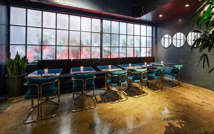 653 Commercial Street — the rear dining room under the previous tenant: factory-pane window wall, brass-framed seating, polished concrete floor.